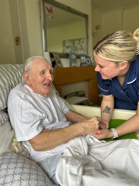 Homecare support holds the hands of a man sat up in bed