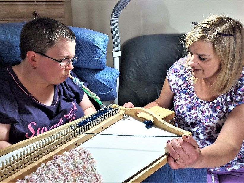 Woman uses mouth tool to knit on a loom support worker direct yarn around the hooks