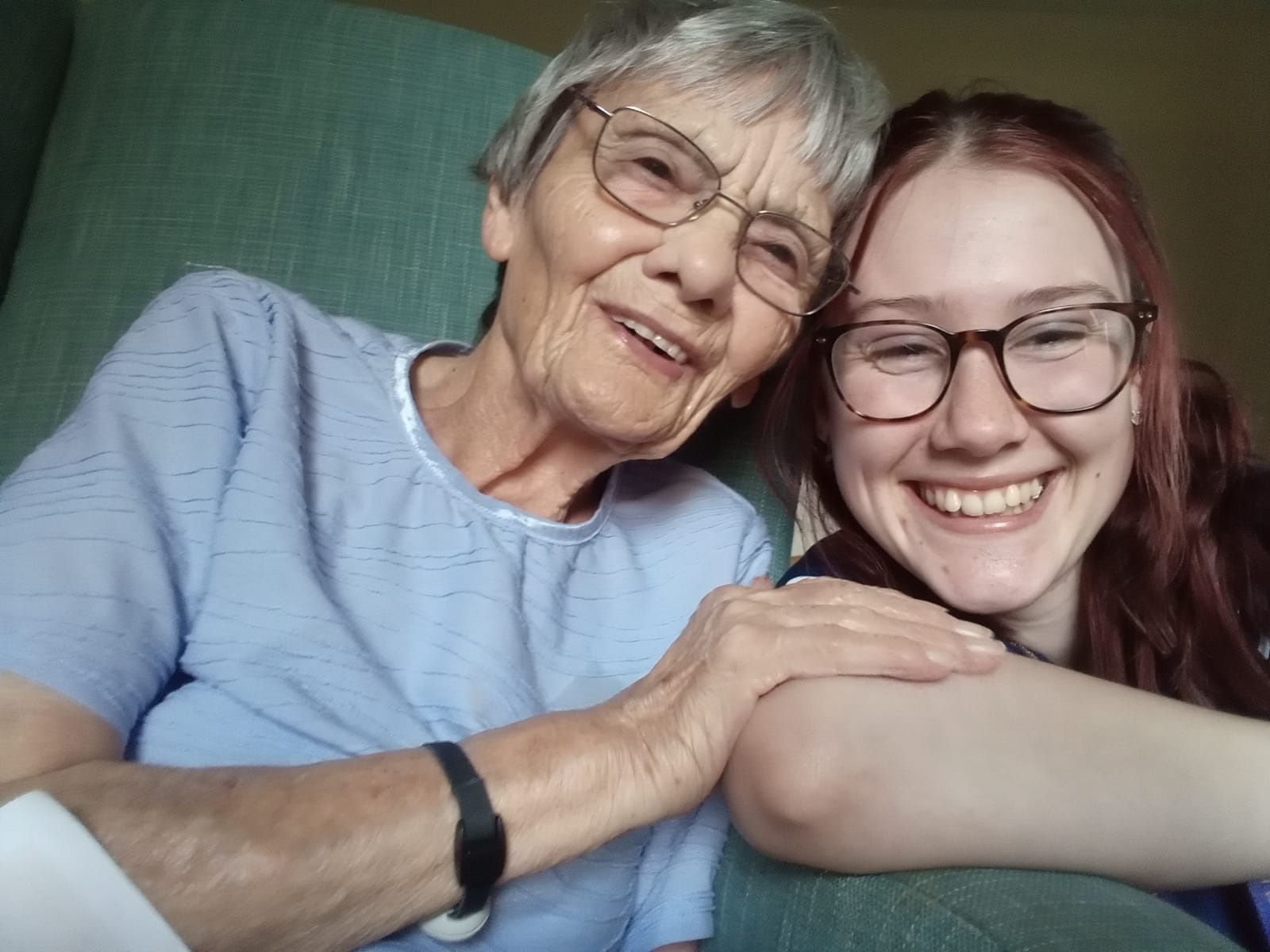 close up shot of homecare worker who sits alongside an older lady both facing the camers and smiling