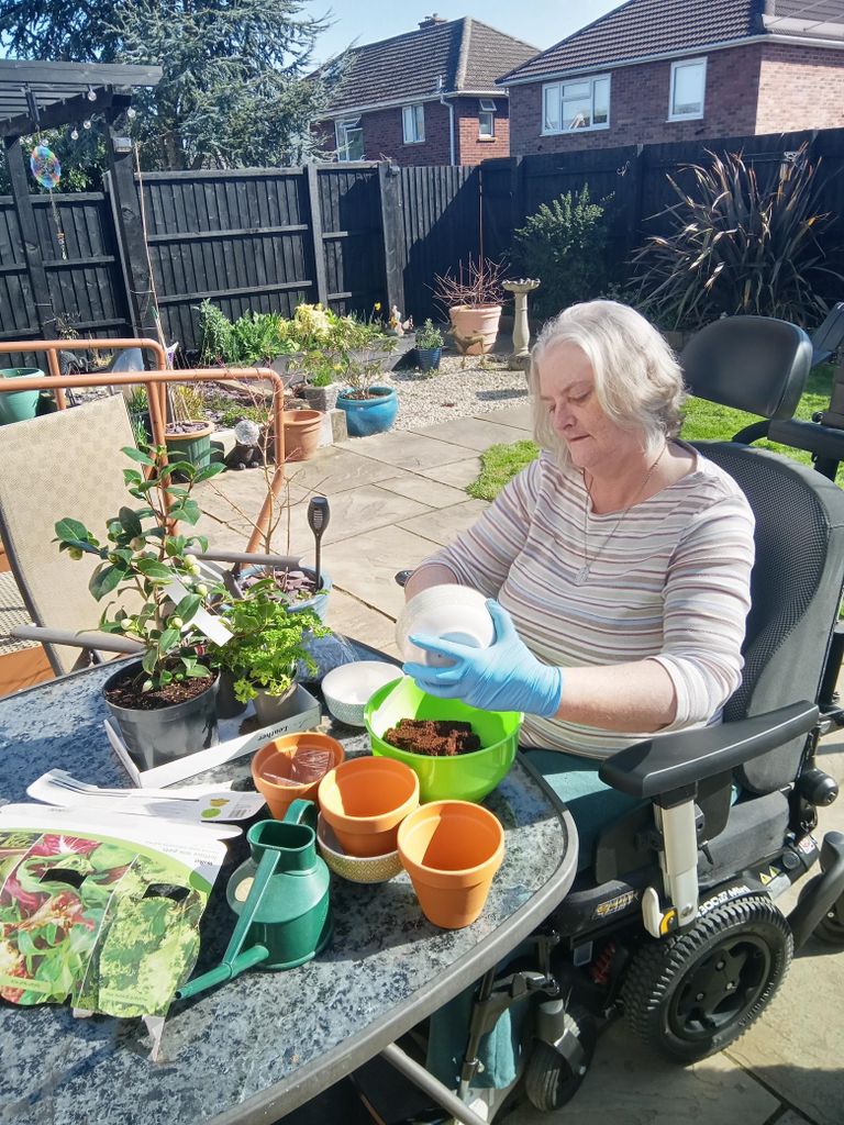 woman seated in a wheelchair enjoying an outdoor gardening session on a patio in sunshine