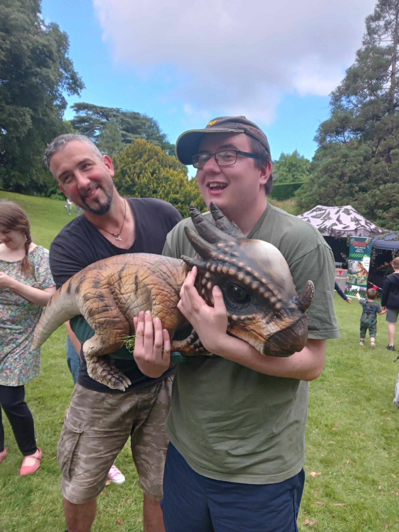 Young man wearing a baseball cap cradles a dinosaur baby puppet in his arms