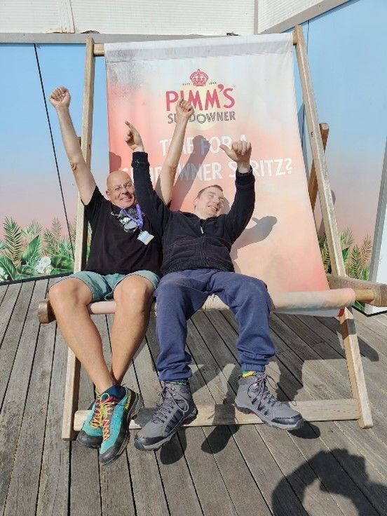 two men sit in an oversized deckchair with their hands raised