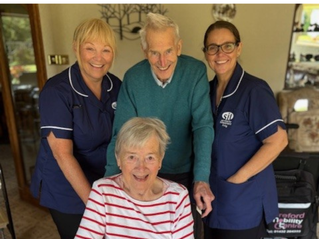 an elderly couple and two Services for Independent Living homecare support workers standing together, all smiling
