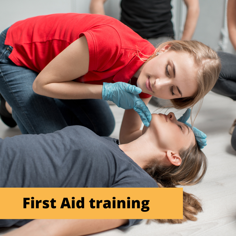 woman kneels beside another woman on the floor tilts head back and listens for signs of breathing.