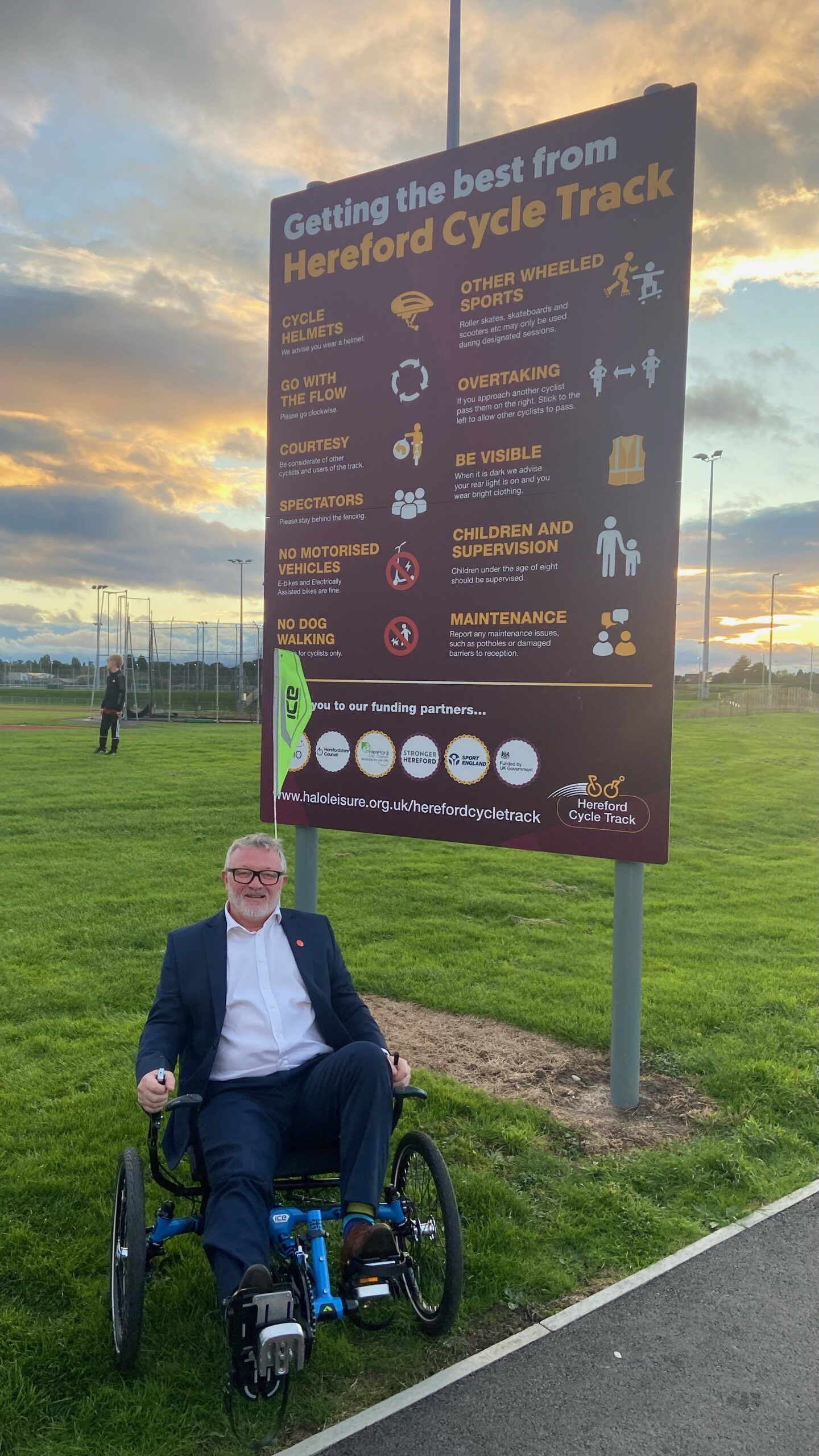 Large outdoor information sign about Hereford Cycle Track with a man seated in a trike by the sign