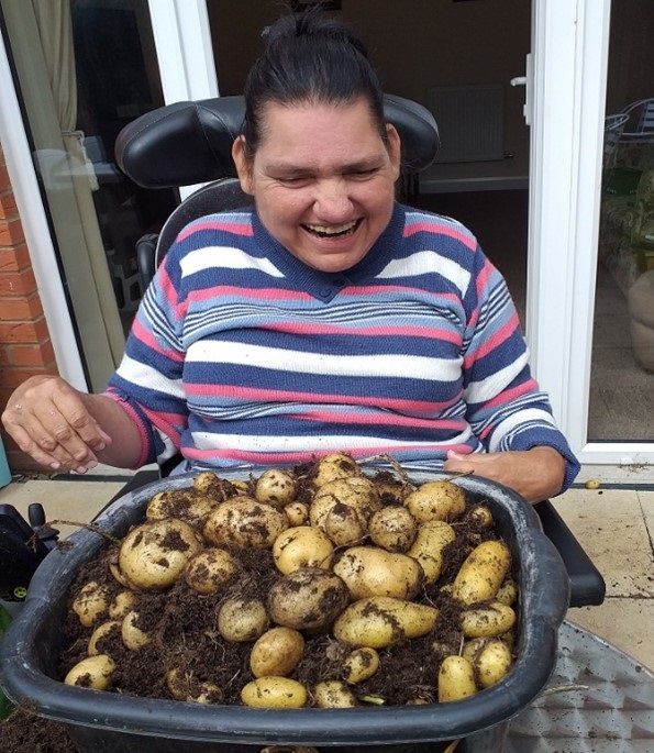 Woman seated in a wheelchair looks pleased holding a bowl of freshly dug potatoes