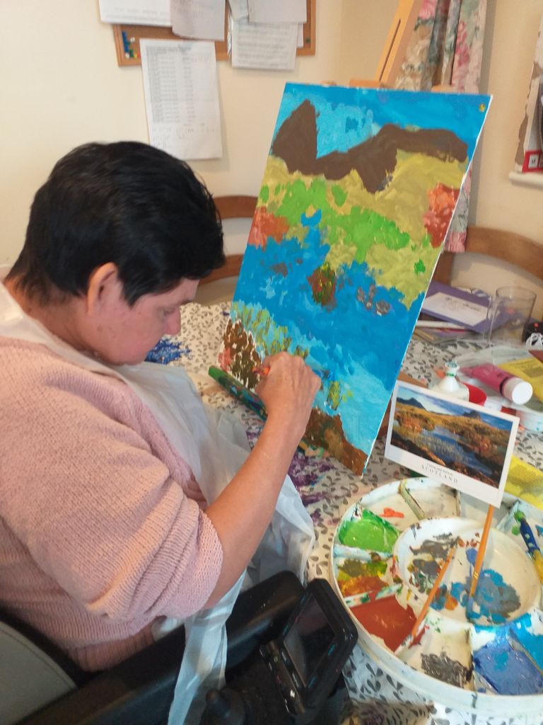 person seated in a wheelchair painting a colourful landscape picture