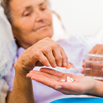 older woman lying in bed takes tablet being offered